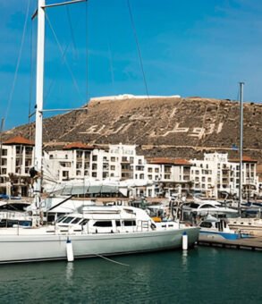 A stunning view of Agadir Marina and the surrounding cityscape, showcasing the modern charm and coastal beauty of this Moroccan gem. Visiting the marina is one of the top things to do in Agadir, offering vibrant cafés, seaside strolls, and breathtaking views of the Atlantic Ocean and city skyline.