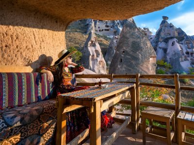 Woman in Bohemian dress sitting on traditional cave house in Cappadocia, Turkey.